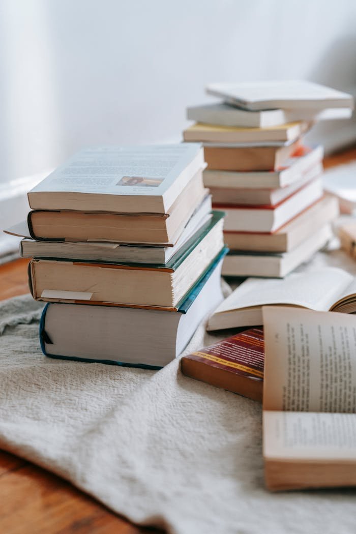 Stack of opened and closed books placed on white soft fabric on floor near wall in light room at home